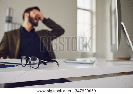 Exhausted Tired Worker At The Workplace Covered His Face With His Hands In The Office