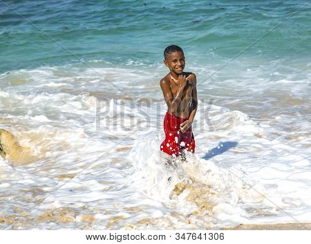 Indonesia, Jayapura, Sentani, 25 August 2019: Smiling Boy Splashing In The Waves Of The Indian Ocean