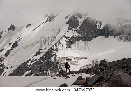 Man With Hiking Equipment Standing On The Rock Around The Snow Remnants