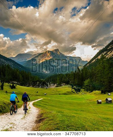 Cycling woman and man riding on bikes in Dolomites mountains andscape. Couple cycling MTB enduro trail track. Outdoor sport activity.