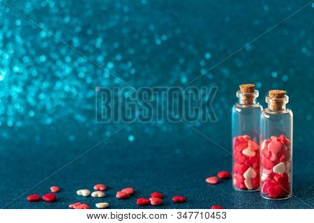 Two Glass Bottles With Heart-shaped Sugar Sprinkles On Gliter Blue Background. Valentines Day Concep