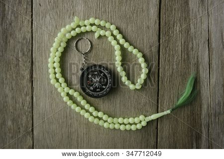 Rosary Beads And Compass On Wooden Background.