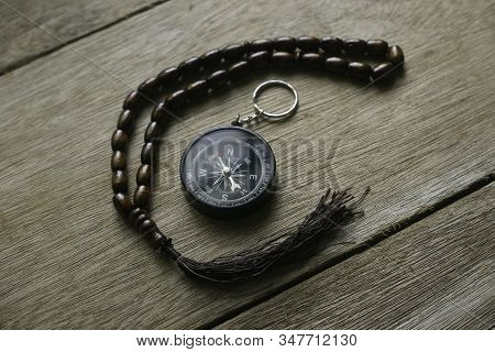 Rosary Beads And Compass On Wooden Background.