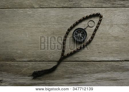 Rosary Beads And Compass On Wooden Background.