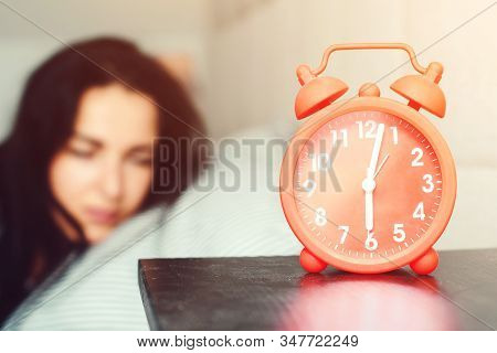 Alarm Clock At Foreground In Bedroom At Home. Young Sleeping Woman In Bed. Early Morning Awakening. 