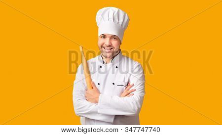 Professional Baker. Happy Chef Man Holding Rolling Pin For Dough Standing On Yellow Studio Backgroun
