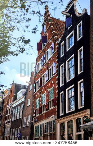 Old Brown Bricky Dutch Buildings In Amsterdam, Netherlands With Bright Sky On Background In Summer D