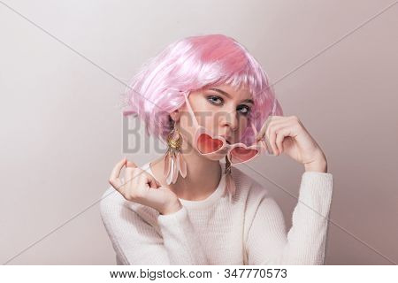 Portrait of teenage model with pink hair posing against pastel background. Studio photo of funky teenager wearing color wig and trendy glasses.