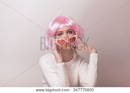 Portrait of teenage model with pink hair posing against pastel background. Studio photo of funky teenager wearing color wig and trendy glasses.