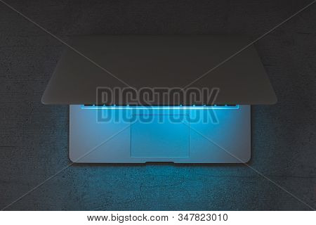 Top View Of A Laptop On A Dark Table, Glowing Blue Screen. Minimalistic Workplace, Working With Comp