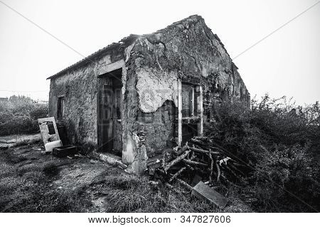 A Wide-angle Black And White Shot Of A Desolate Stone House With Rough Flaked Walls Covered With Cem