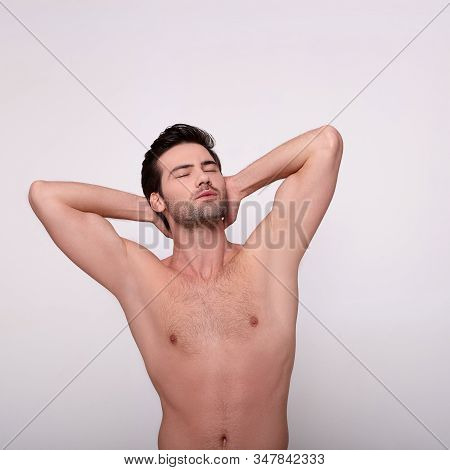 An Image Of A Charming Topless Guy Standing Against A Light Background And Showing Off His Smooth Ar