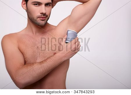A Handsome Young White Naked Man, With Dark Eyes And A Beard, Applies Deodorant To His Armpit And Lo