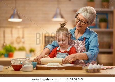 Happy loving family are preparing bakery together. Granny and child are cooking cookies and having fun in the kitchen. Homemade food and little helper.                               