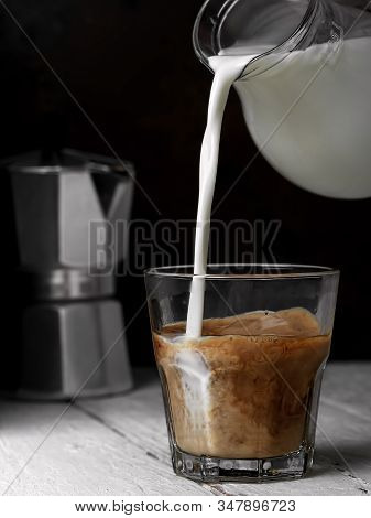 Glass With Espresso And Milk On The White Wooden Background. Milk Is Poured Into A Glass Of Coffee. 