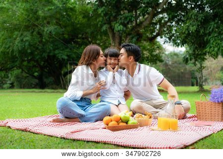 Asian Teen Family Happy Holiday Picnic Moment In The Park With Father, Mother Kissing Daughter Looki