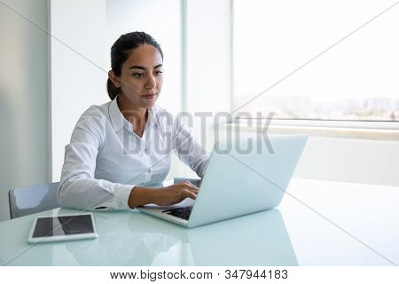 Serious Young Businesswoman Using Laptop In Office. Focused Young Businesswoman Sitting At Desk And 