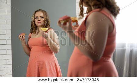 Depressed Overweight Female Eating Donuts In Front Of Mirror, Eating Disorder