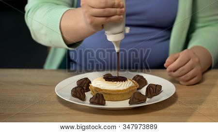 Overweight Female Pouring Lots Of Chocolate Dressing Over Pastry, Obesity Issue