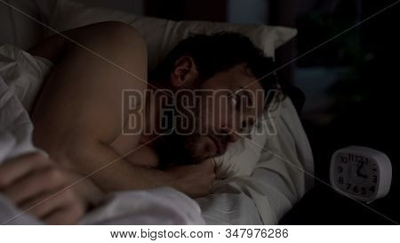 Annoyed Guy In Bed Unable To Fall Asleep, Looking Angrily At Clock, Insomnia