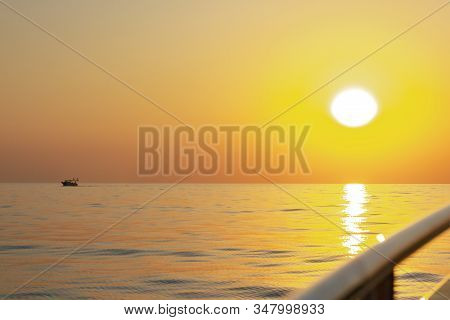 Silhouettes Of Fishermen Against A Bright Sunset With A Large Yellow Sun Under The Surface Of The Se