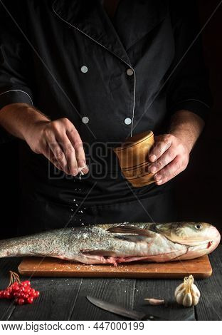 Cook Prepares Silver Carp Herring In The Restaurant Kitchen. Chef Sprinkles Salt On Fish. Work Envir