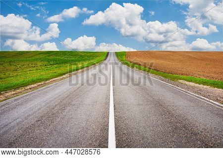 Asphalt Road Leading To Horizon Through Green Agricultural Fields At Summer Day With Blue Clody Sky,