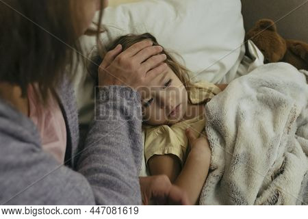Portrait Of Sad Engrossed Sick Little Girl And Her Mother Touching Daughters Forehead.