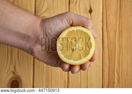 Juicy Yellow Lemon In Man Hand On Wood Background Close Up