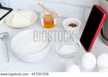 The Concept Of Online Lessons In The Preparation Of Cookies. A Smartphone In A Red Case And Ingredie
