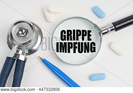 On A White Surface Lie Pills, A Pen, A Stethoscope And A Magnifying Glass With The Inscription - Gri