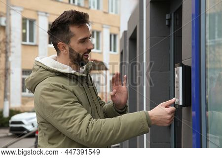 Happy Man Ringing Intercom While Waving To Camera Near Building Entrance