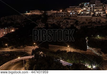 Night View Over The Mellieha Bay In Malta With The Mediterranean Sea, Houses And Rock Structures