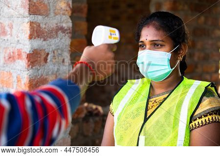 Shoulder Shot Of Man Checking Body Tempreture Of Woman Worker With Medical Face Mask At Workplace - 