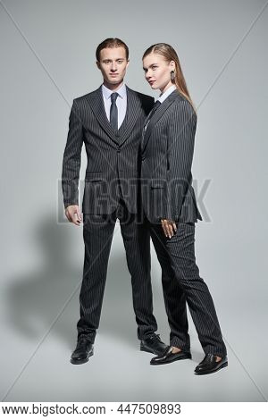Fashion shoot. Full length portrait of stylish young man and woman in elegant striped pantsuits on a gray background. Impeccable look. Men's clothing style. 