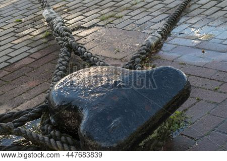 A Wet Mooring Bollard Painted Black, With Three Thick Braided Mooring Ropes Of Moored Vessels Attach