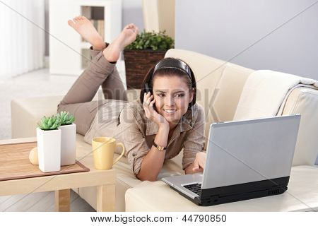 Sorridente ragazza in chat sul telefono cellulare, utilizzando il computer, posa sul divano, sorridente.