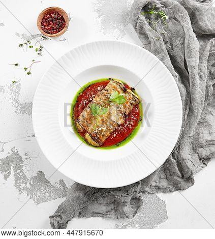 Eggplant rolls stuffed with tomato and cheese. Baked eggplant and cheese rollatini. Eggplant appetizer in white plate on stone background. Plant-based menu