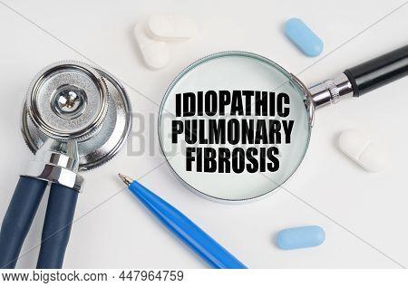 On A White Surface Lie Pills, A Stethoscope And A Magnifying Glass With The Inscription - Idiopathic
