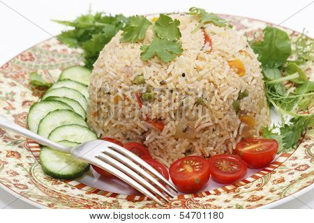 A healthy tomato (thakkali) biriyani with a salad of cucumber, cherry tomatoes and some fresh leaves, closeup with a fork. This biryani is a South Indian dish.