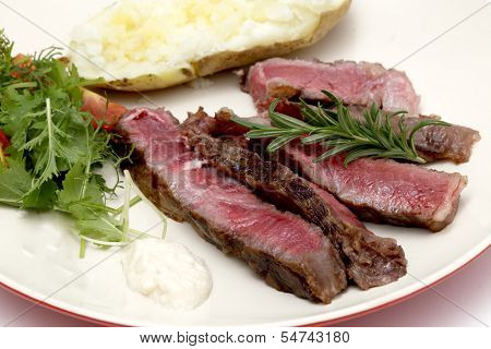 Closeup on slices of grilled gourmet wagyu rib-eye steak served with horseradish sauce, a baked potato and a fresh green salad
