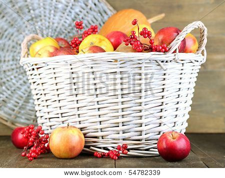 Juicy apples and pumpkin in wooden basket on table close-up