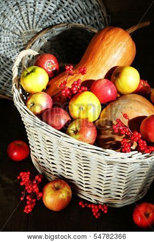 Juicy apples and pumpkin in wooden basket on table close-up