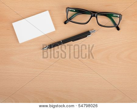 Blank business cards with pen and glasses on wooden office table with copy space