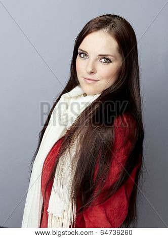 Portrait of a young smiling casual woman with long brunette hair on gray studio background, wearing red suede leather jacket and white scarf 