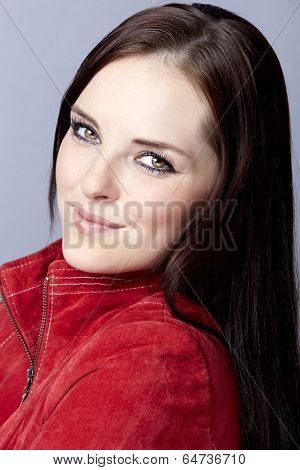 Portrait of a young business woman on gray studio background, wearing red suede leather jacket with long brunette hair