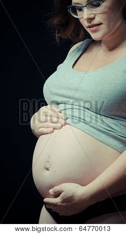 pregnant woman on black background with hands on her belly