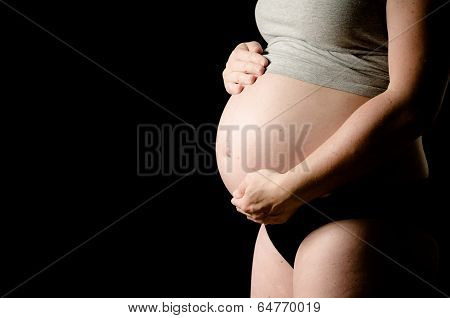 pregnant woman on black background with hands on her belly