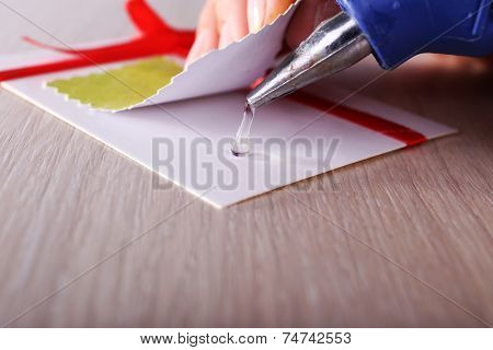 Woman's hand making postcard with red ribbon and bow with a help of glue gun
