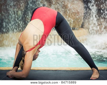 Woman practicing yoga near waterfall. Wide-Legged Forward Bend. Parsva Prasarita Padottanasana